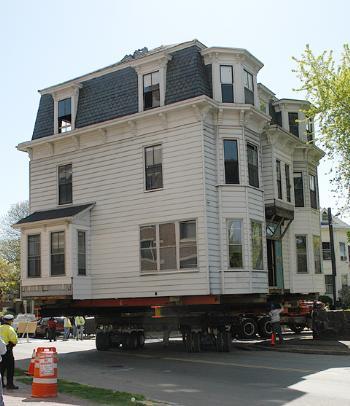 Construction workers load a Victorian house from Prescott Street—where Harvard is planning to build its new Center for Government and International Studies—onto wheels, for the journey to a new home.