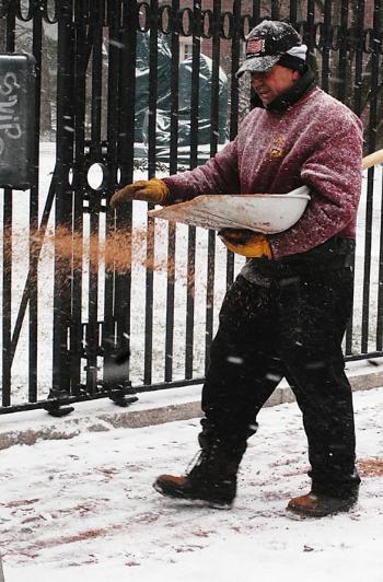 A Harvard worker spreads sand along a sidewalk on Quincy Street as snow blanketed the Northeast yesterday.