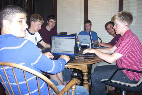 Zuckerberg, back, head of table, and his team of programmers, including Dustin A. Moskovitz '06-'07, left, do their business casually at the kitchen table in Palo Alto, Cal. the summer after founding thefacebook and leaving Harvard.