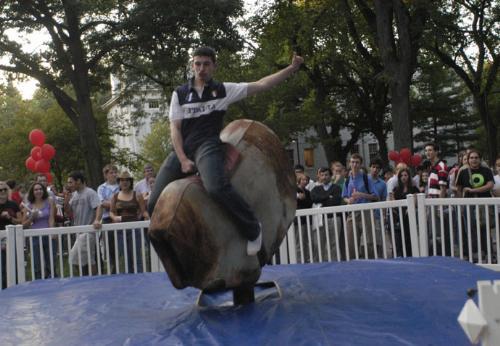 Students line up to ride the mechanical bull, while crowds of spectators form.