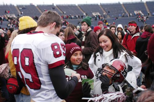 Senior wide receiver Matthew T. Lagace signs an autograph and lends his helmet to an admiring young fan on the field after the game.