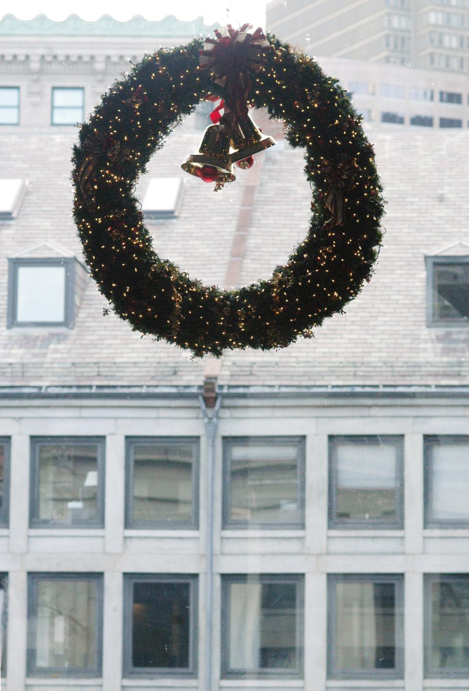 A holiday wreath decorated with lights and bells glitters in a window of the Quincy Market rotunda, merrily facing the historic buildings of Boston.