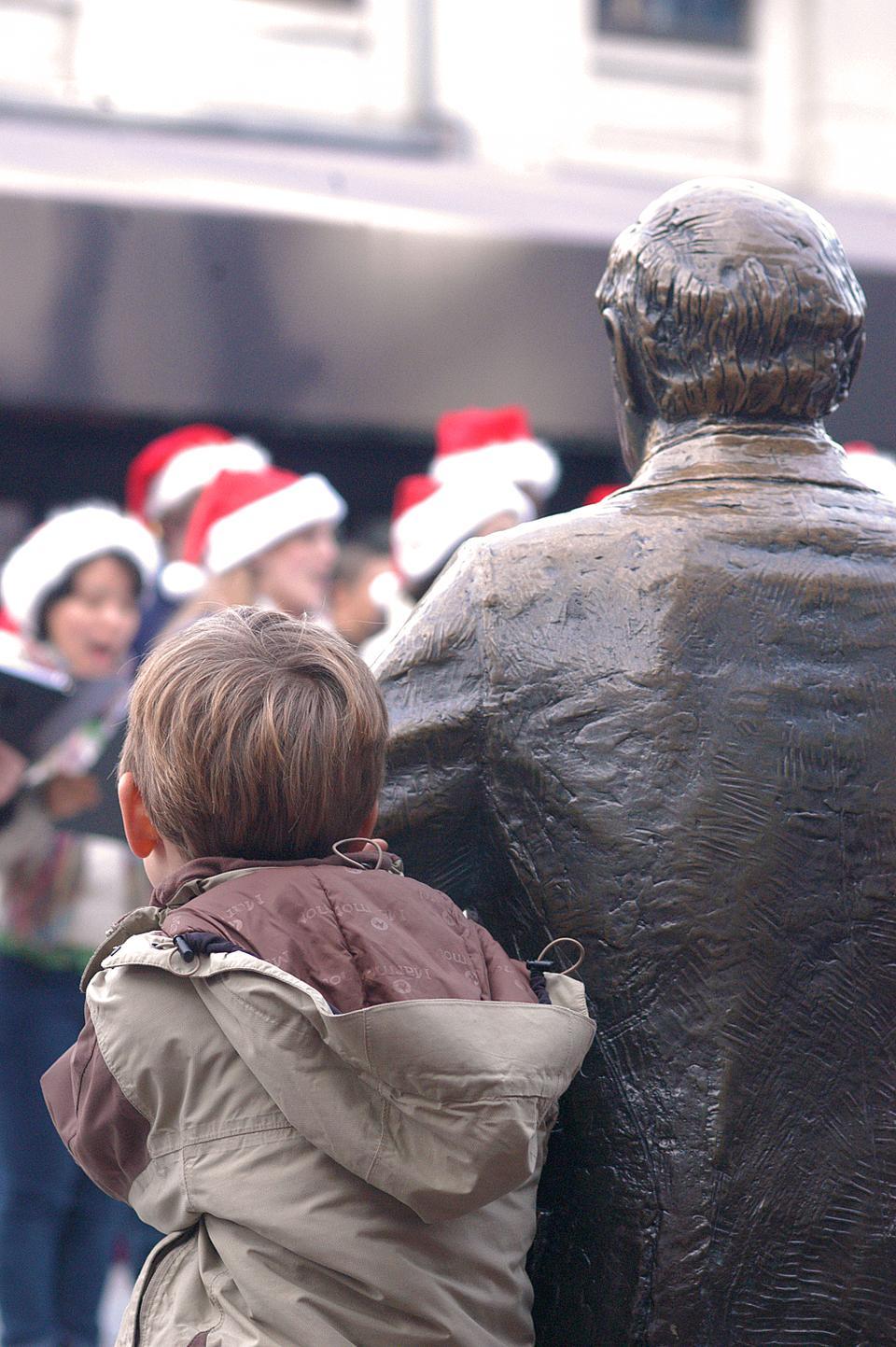 A young boy peeks out from behind a statue as choir singers serenade passerbys during an annual festival to celebrate the upcoming holidays in Boston.