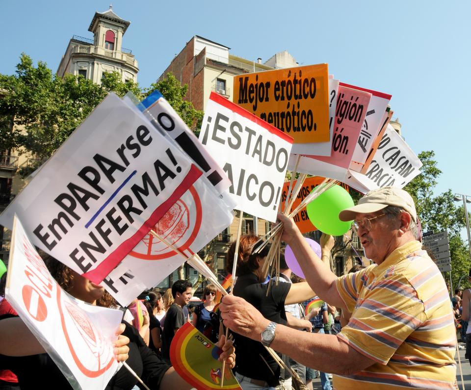 A man distributes signs for participants to carry during the Barcelona Gay Pride Parade.