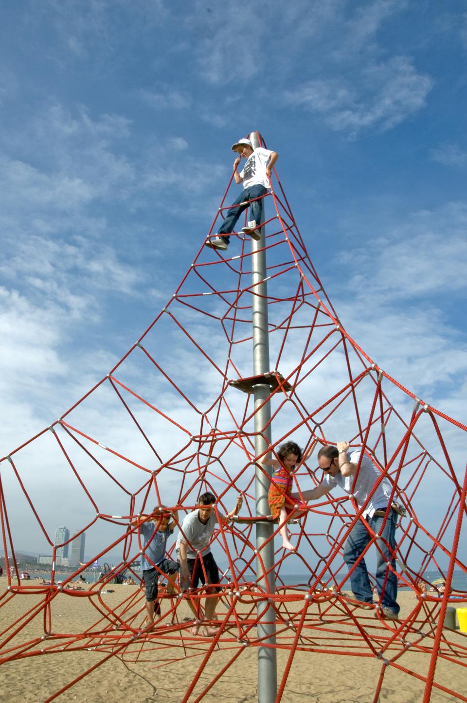 Children and the occasional adult enjoy a sunny day and play on this structure located on Barcelona's beach.