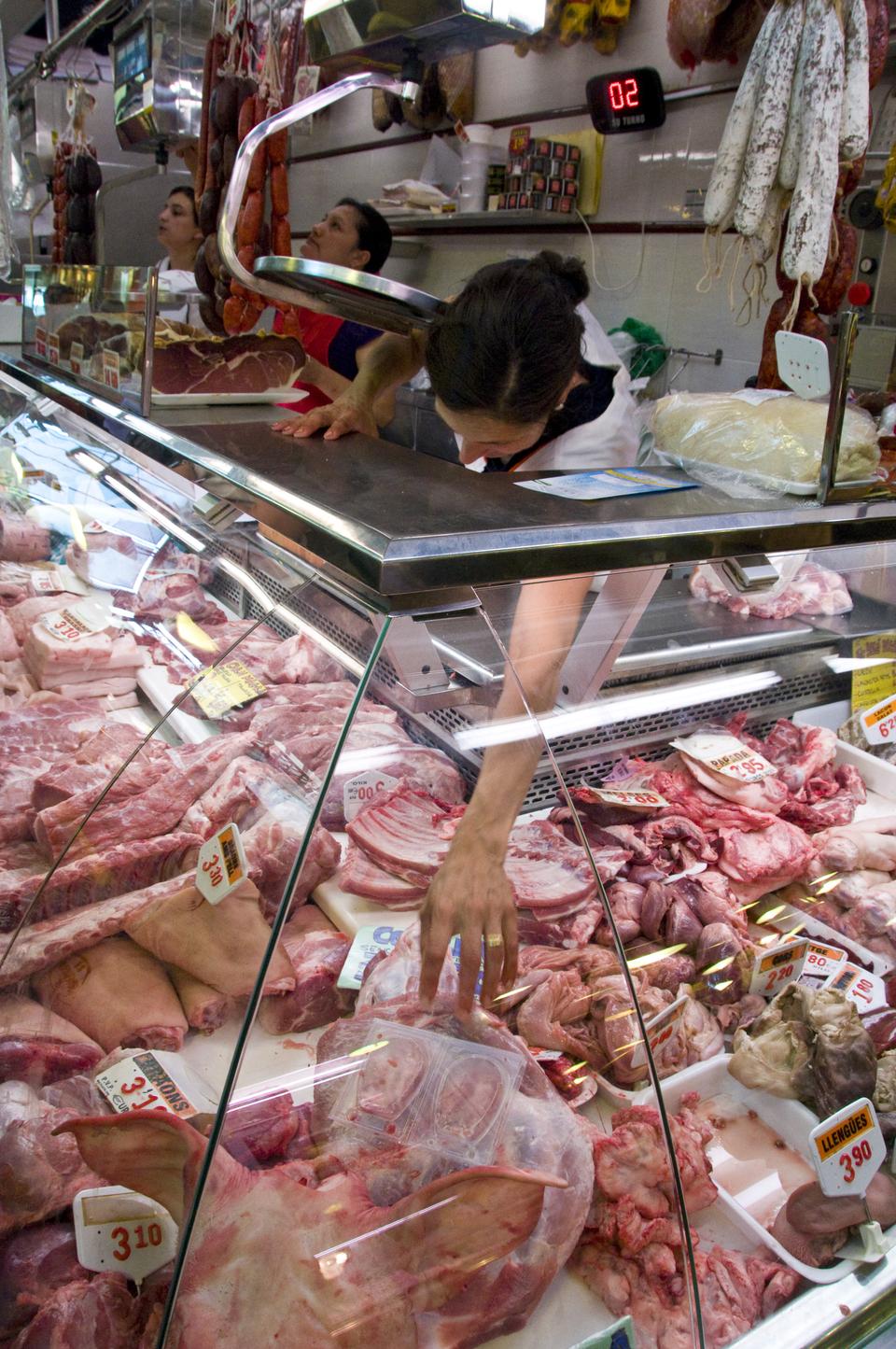 A woman reaches for a slab of meat in the Boqueria.  Although the market is a popular tourist attraction, locals come here as well to enjoy the fresh meat and produce.