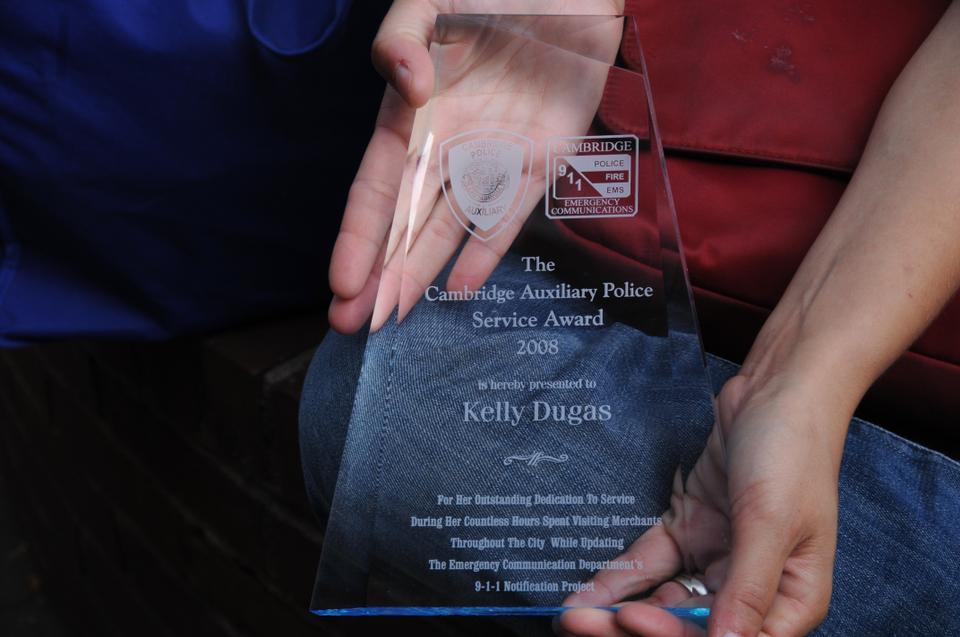 Kelly Dugas Coveney, member of the Chair Club since 2006. shows an award she received from the Cambridge Police Department for collecting emergency callback numbers from city businesses. 
