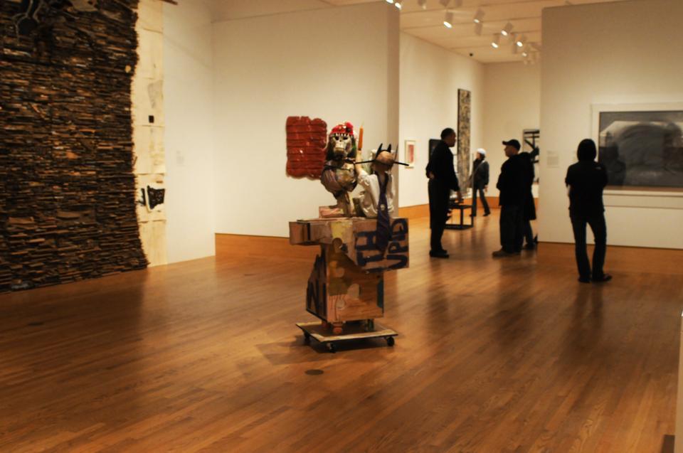 Several viewers look at exhibits in the modern and contemporary art section. In the center is a piece titled "I'm With Stupid" by Rachel Harrison.