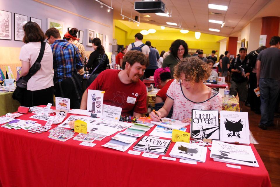Eric Boeker, a comic designer whose work is based on a world where humans and zombies live in peaceful harmony, looks over at the work of his stand partner at the Massachusetts Independent Comics Expo.