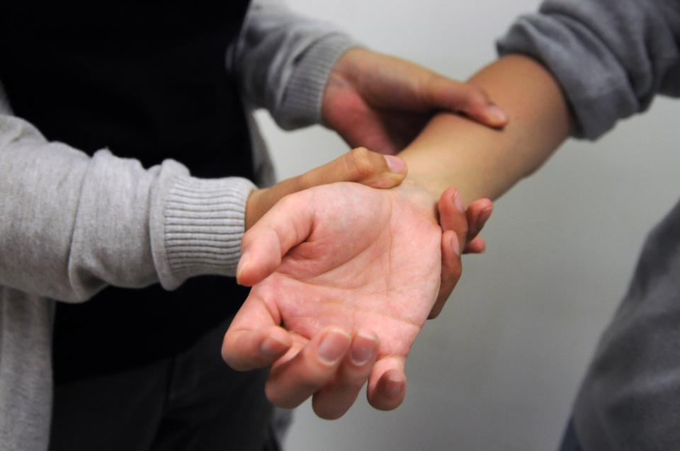 While holding up the person’s wrist, use your thumb to massage his or her forearm. 