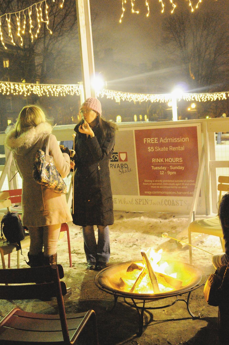 Two women enjoy free roasted marshmallows on friday night in front of the ice rink in the new fallen snow.