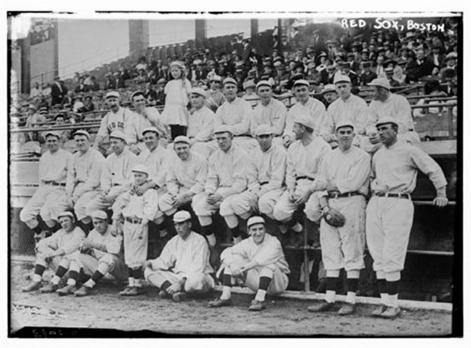 The 1912 Boston Red Sox pose in front of their dugout at Fenway Park. Top row (left to right): Quirk (trainer), Speaker, Joe Wood's sister Zoe, Wood, Cady, Thomas, O'Brien, Bradley, Lewis. Middle row: Hooper, Carrigan, Yerkes, Henriksen, Engle, Nunamaker, Hall, Gardner, Collins, Stahl. Front row: Wagner, Bedient, mascot, Pape, Krug.