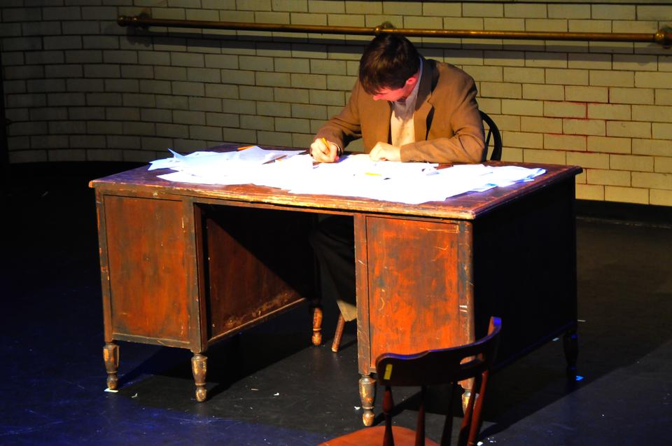 Sitting at the desk is Peter Bestoso, playing the part of "The Man", in Monstrous Doubles, a student-written play performed at Adam's Pool Theatre.