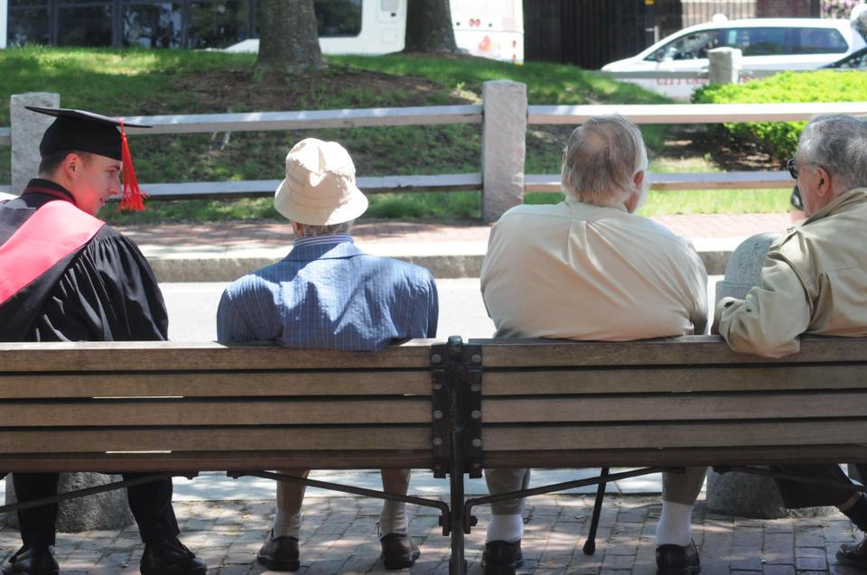 A graduate sits on a park bench with some elderly gentlemen after the Morning Exercises on Thursday.