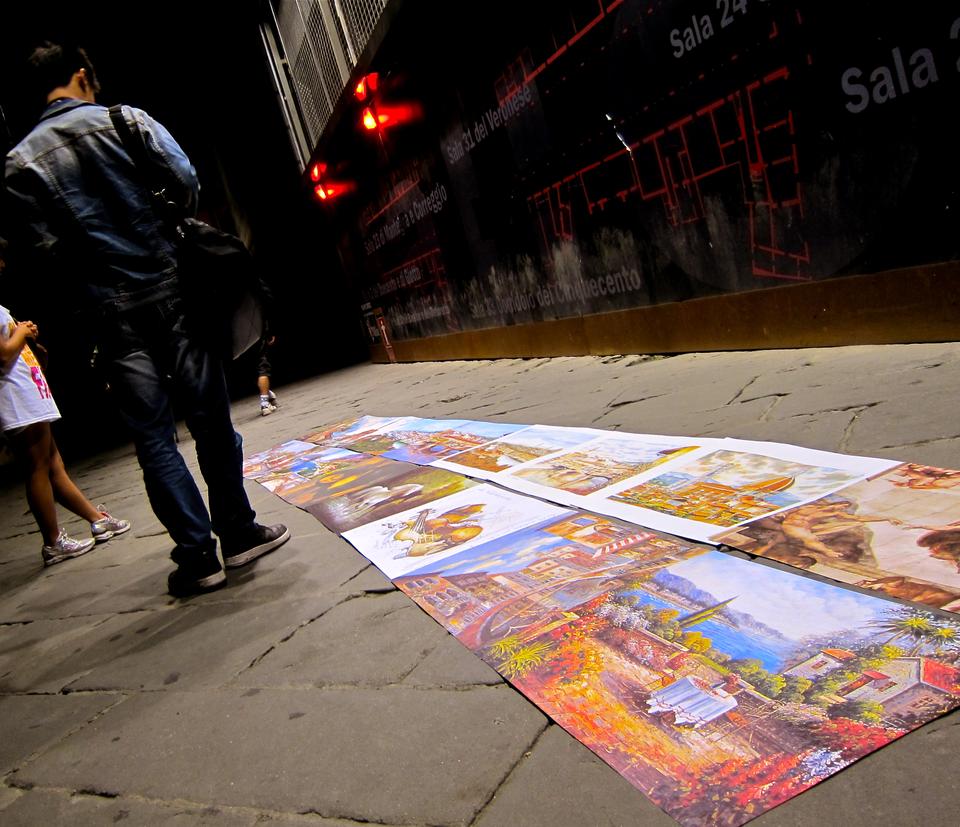 Caption for the photo: A visitor to Florence pauses to admire the tourist fare lined along a street near the Arno River during a nighttime stroll. 