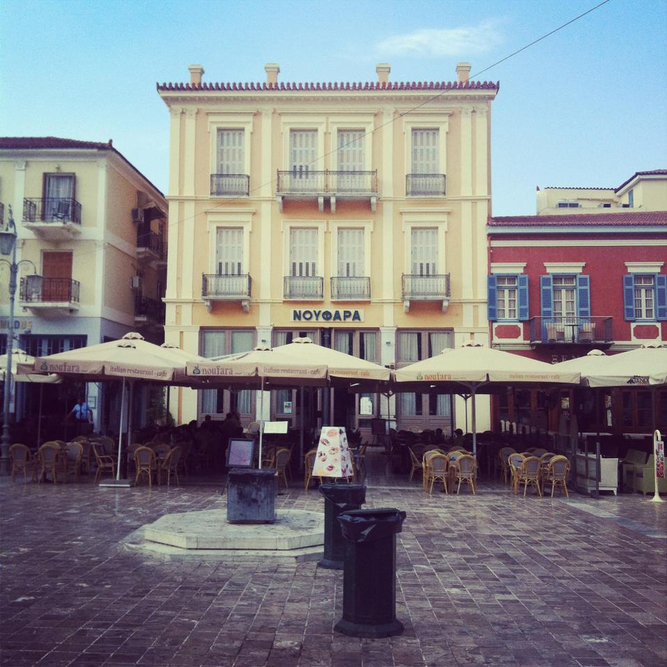 Cafés in a square in Nafplio with few customers. 