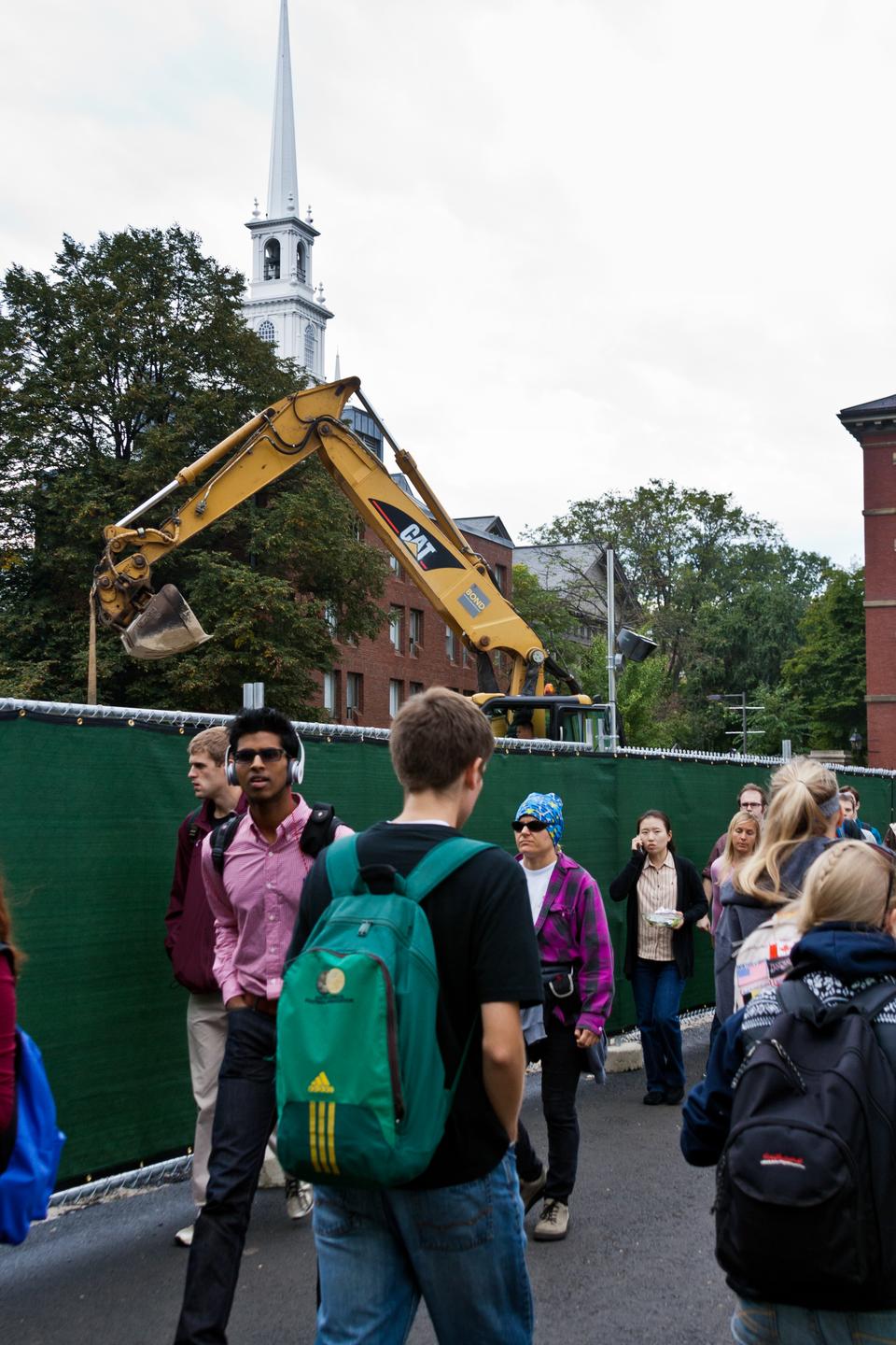 Students walk through the narrow passage in front of the Science Center as the construction work goes on. Harvard is transforming the plaza outside the Science Center as a part of the Common Spaces initiative.