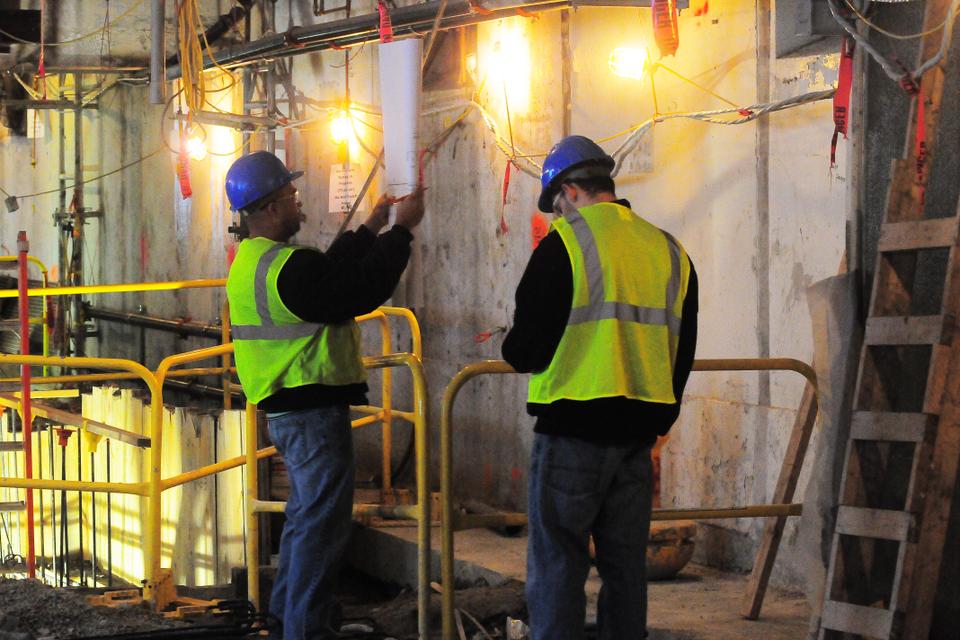Two construction workers are trying to figure out the right way for Quincy's intricate plumbing system.  