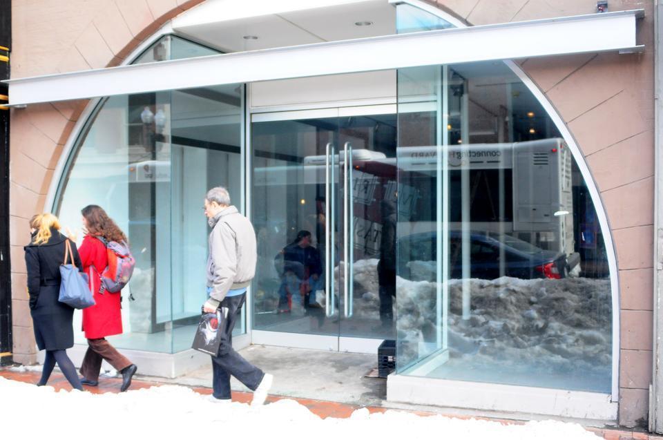 Pedestrians in Harvard Square walk by a worker sitting inside the soon-to-be YougurtLand shop at 24 JKF street. 