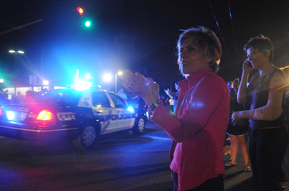 An onlooker applauds as police units withdraw from the scene of Dzhokhar Tsarnaev's capture in Watertown friday evening. Neighborhood residents lined Mt. Auburn St. to recognize emergency officials as they left the scene.
