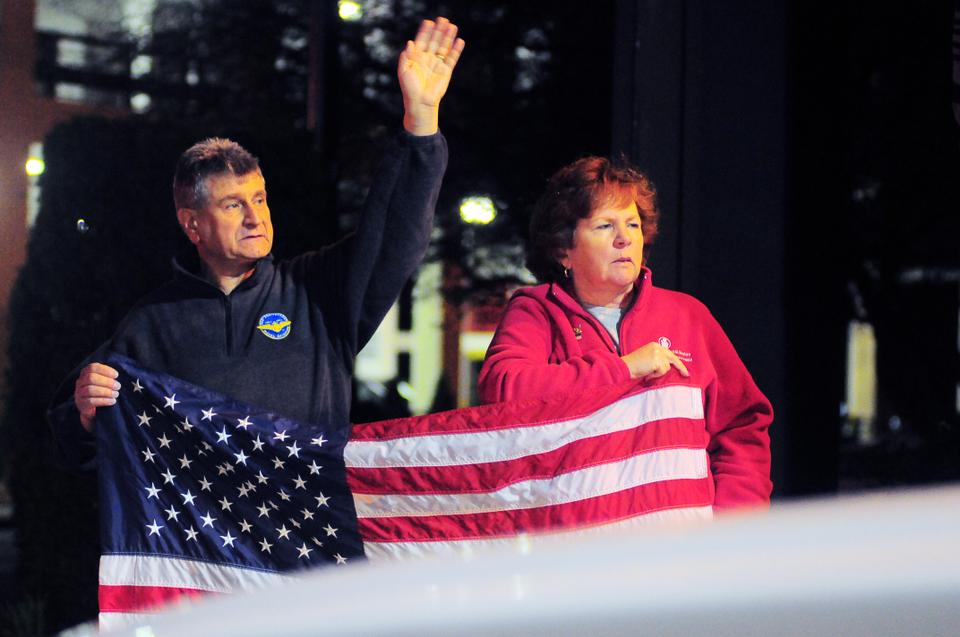 A couple waves to passing police officers while holding a flag on Arsenal St. in Watertown on Friday night as emergency personnel departed from the scene. About an hour earlier, authorities had announced the capture of Boston Marathon bombing suspect Dzhokhar Tsarnaev.