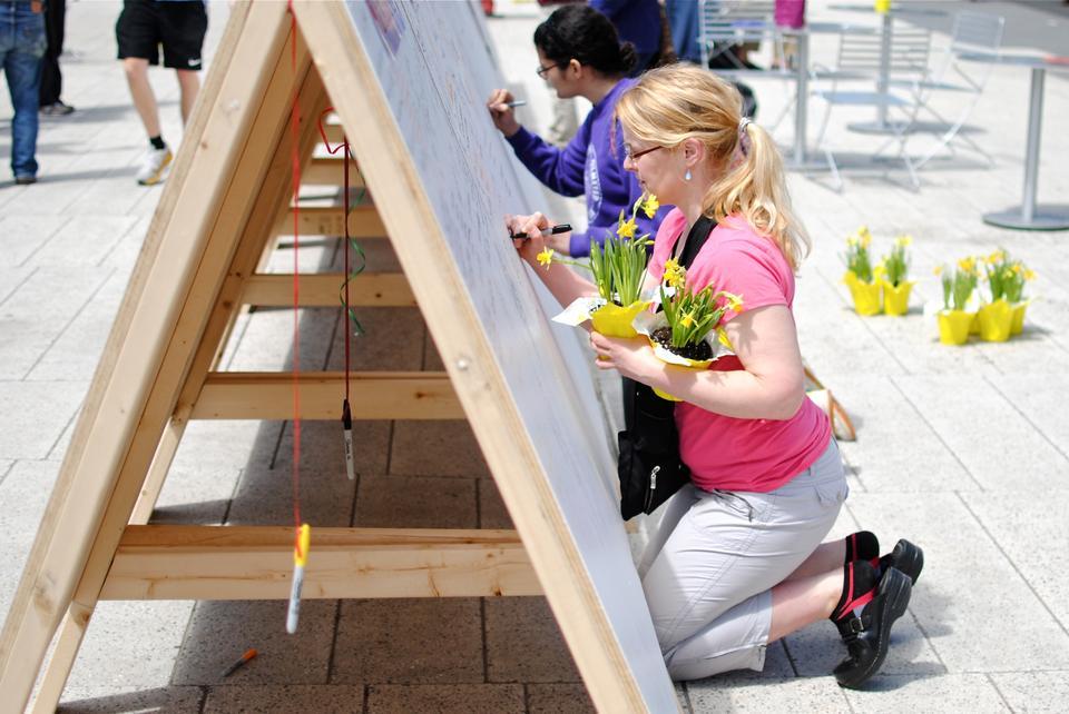 A woman writes on the "Boston Strong" wall that sits on the newly renovated Science Center Plaza. The wall provides a space for Harvard affiliates to write notes to those affected by the Marathon Bombings, and to give thanks. 