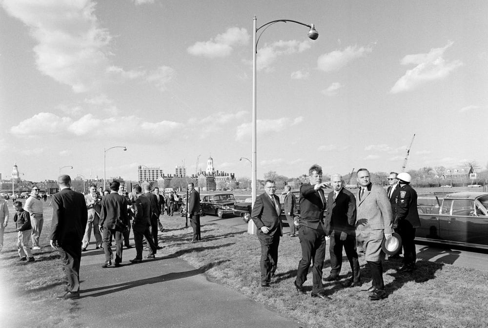 President John F. Kennedy ‘40 motions with his arm towards the proposed site of his future Presidential Library, along the banks of the Charles River in Boston, with Eliot House and Dunster House visible in the horizon.