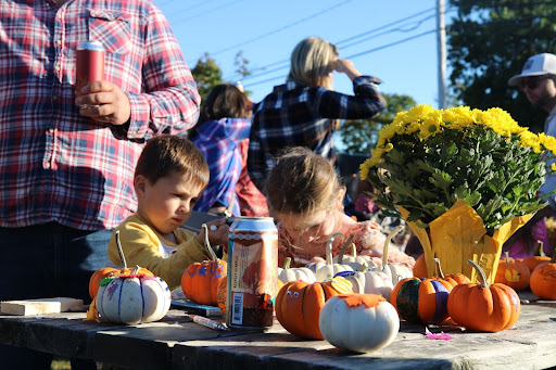 Young children paint pumpkins as their dad stands closely behind socializing.