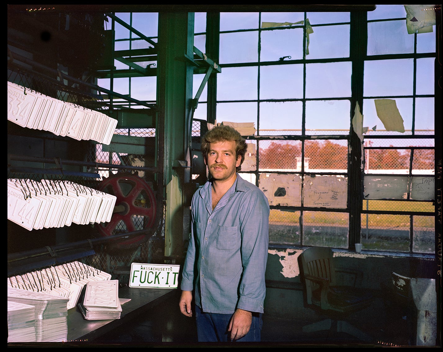 A man incarcerated at Walpole stands beside license plates manufactured at the prison in the early 1980s. At the time, Walpole produced every license plate in the state of Massachusetts. Production has since moved to the neighboring MCI-Norfolk.