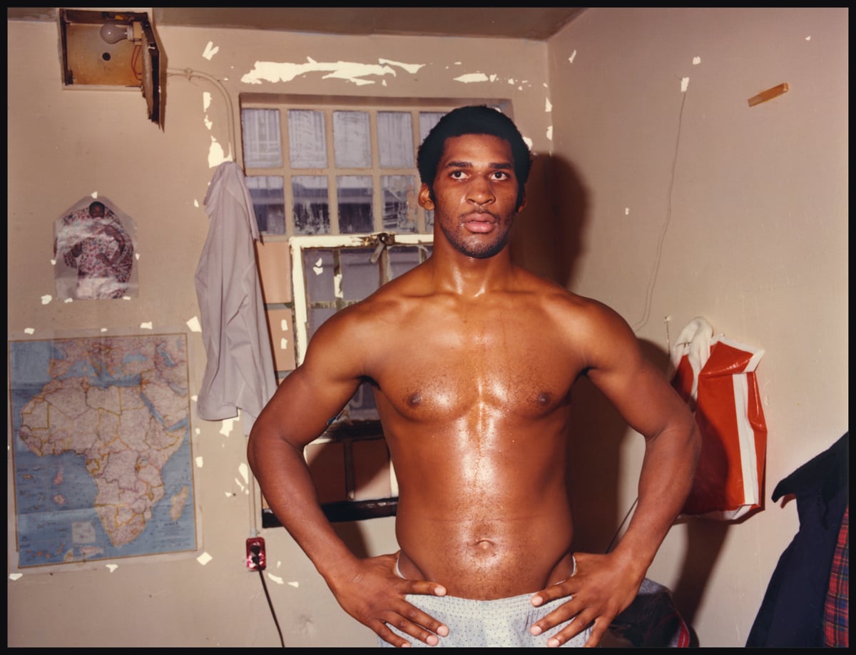 A man incarcerated at Walpole stands in his cell, with a map of Africa on the wall behind him.