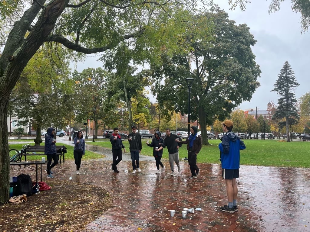 Contestants of Harvard Survivor hold cups on a flat extended hand while balancing on one foot.
