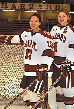 Angela Ruggiero and Julie Chu pose in their Harvard jerseys in the Bright-Landry Hockey Center. Both players won the Patty Kazmaier Award, and both are Olympians. 